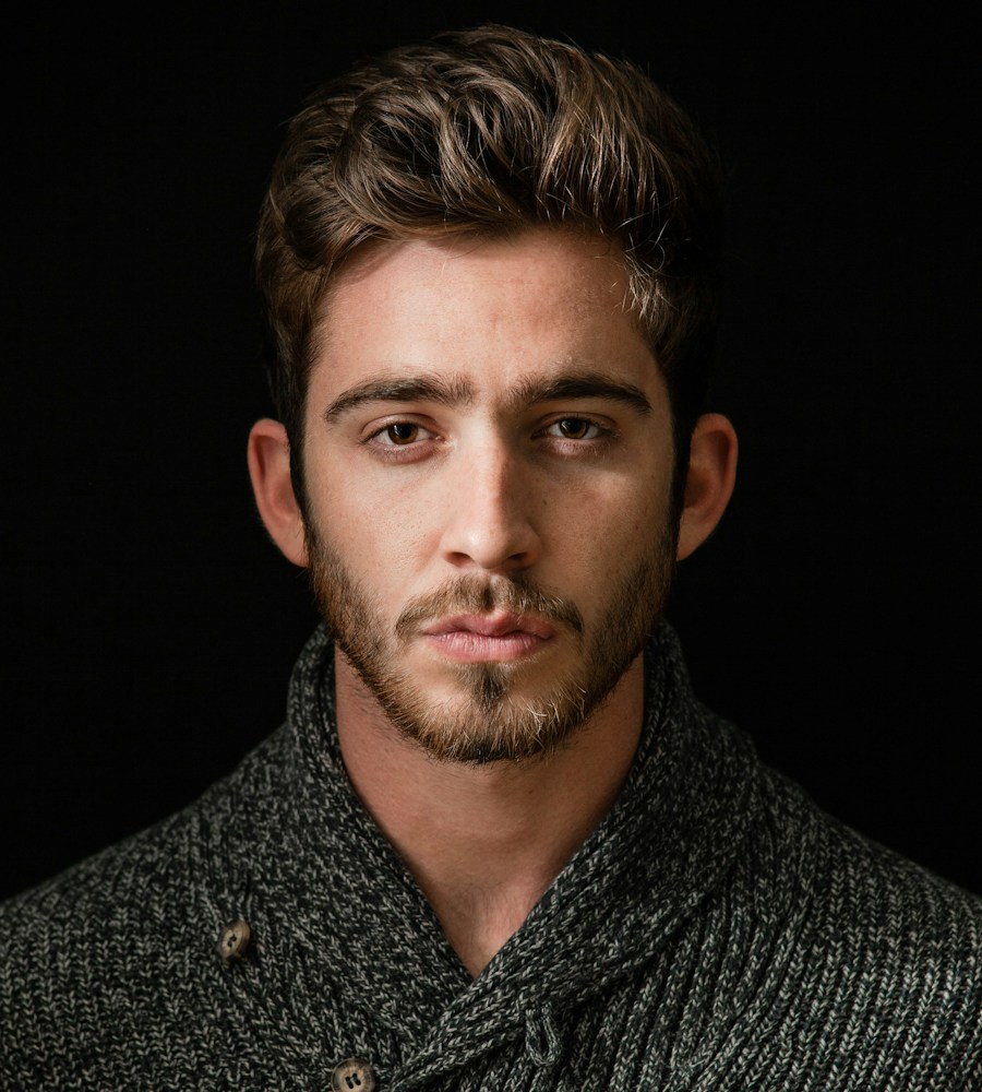 A man's portrait in a dark patterned shirt against a black background